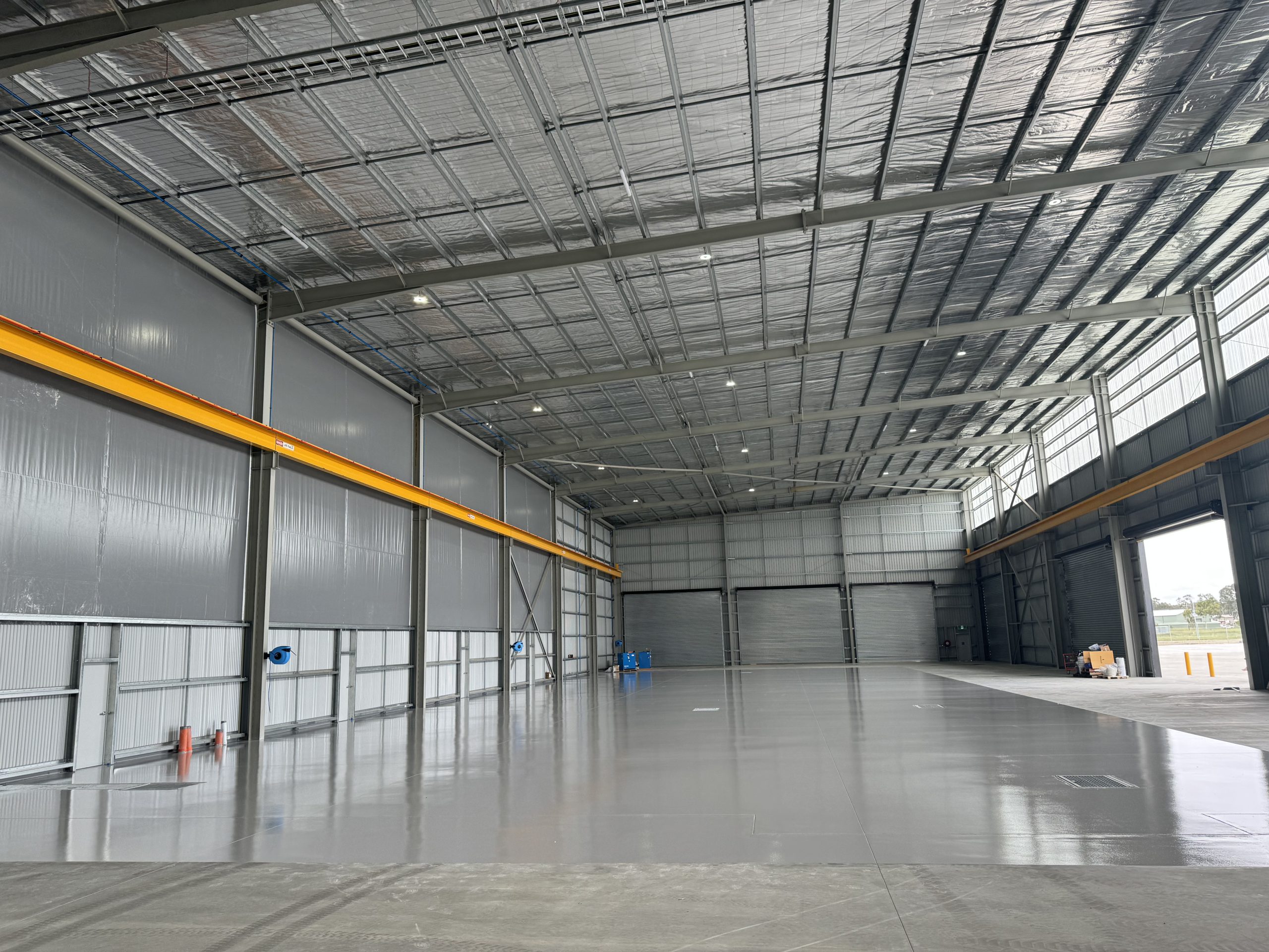 Wide-angle view of grey epoxy floor coating in large aircraft hangar with yellow overhead crane beam
