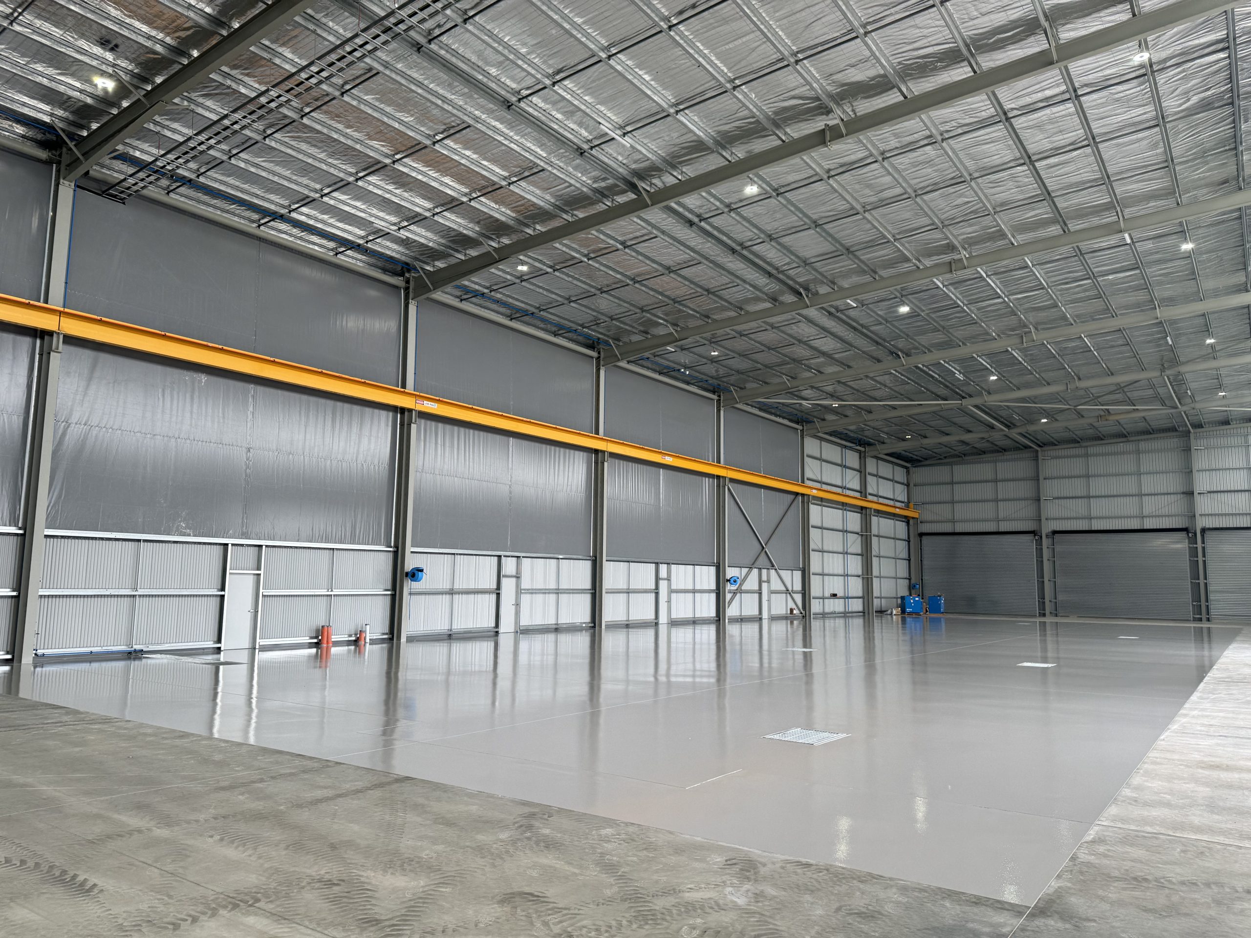 High-gloss grey epoxy floor coating in large industrial aircraft hangar with overhead crane beam
