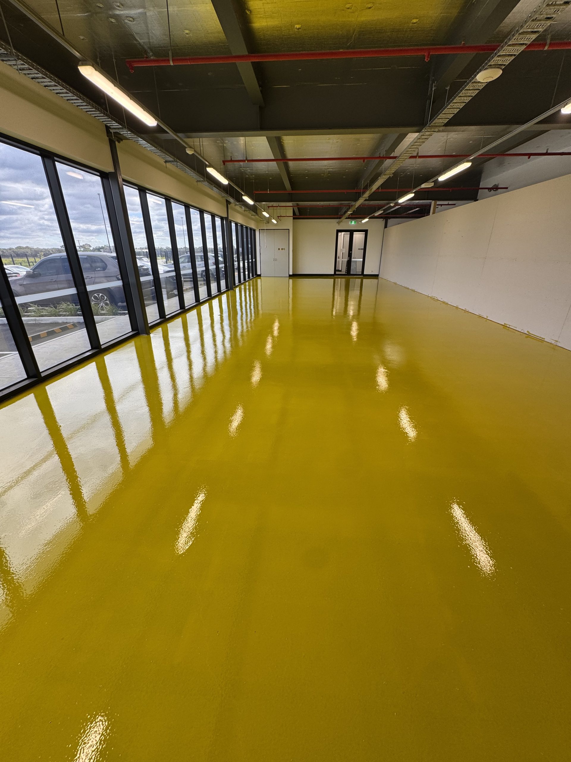 Mirror-finish yellow epoxy floor coating in large commercial space with floor-to-ceiling windows