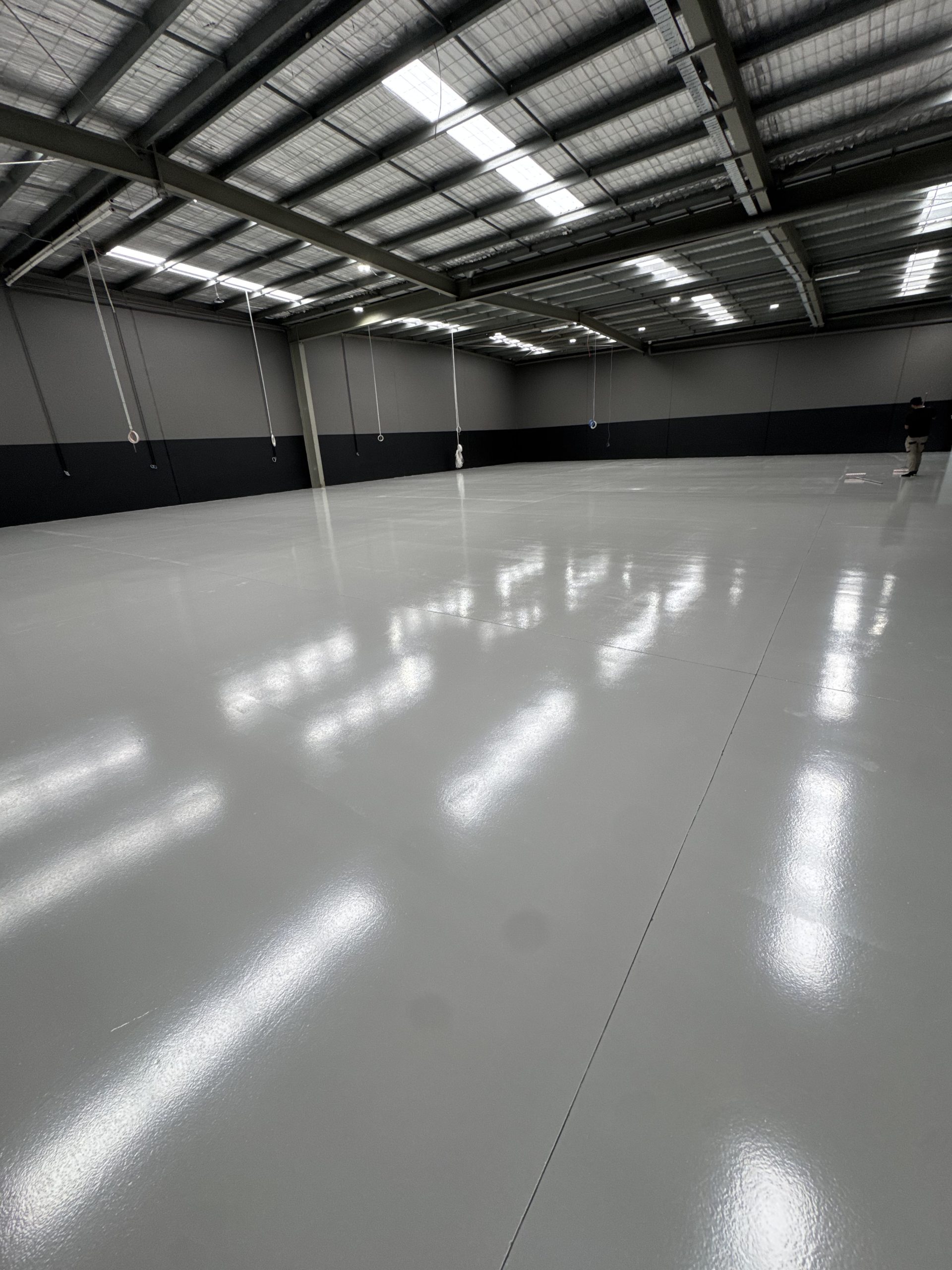 Expansive light grey epoxy floor coating in commercial gymnasium with suspended gymnastics rings