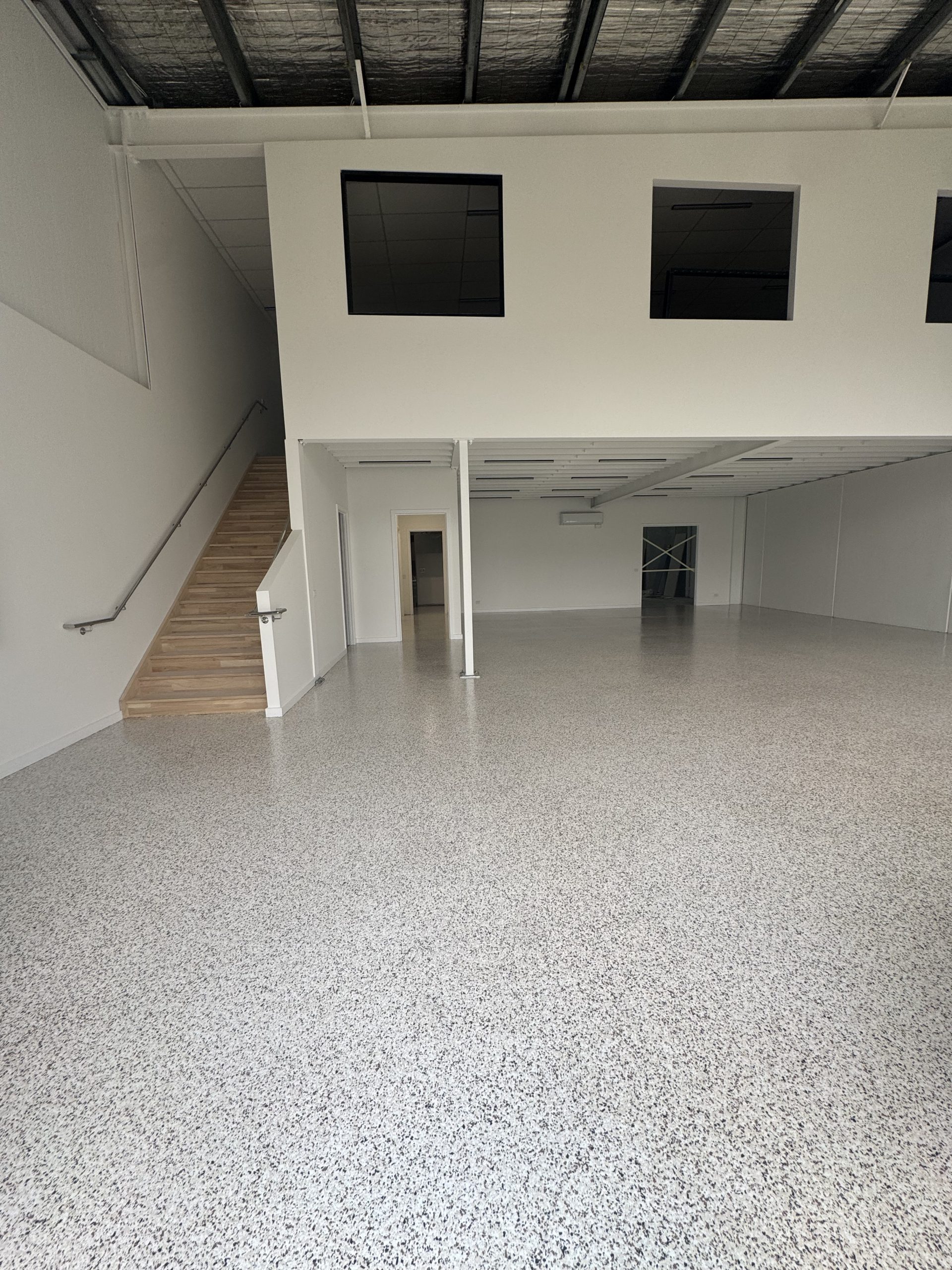 Epoxy flake floor coating in commercial warehouse with mezzanine level, timber staircase and white walls