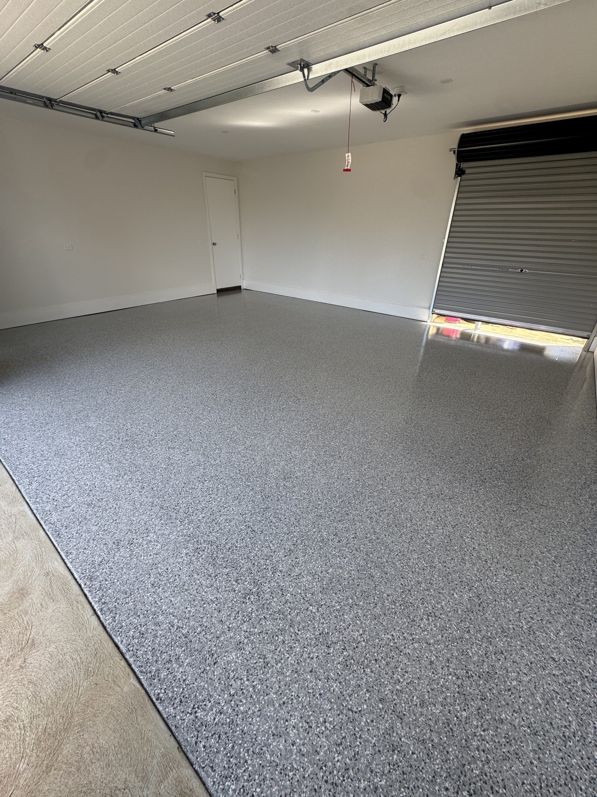 Clean new build garage with mid-grey epoxy flake floor coating, white walls, and partially open roller door