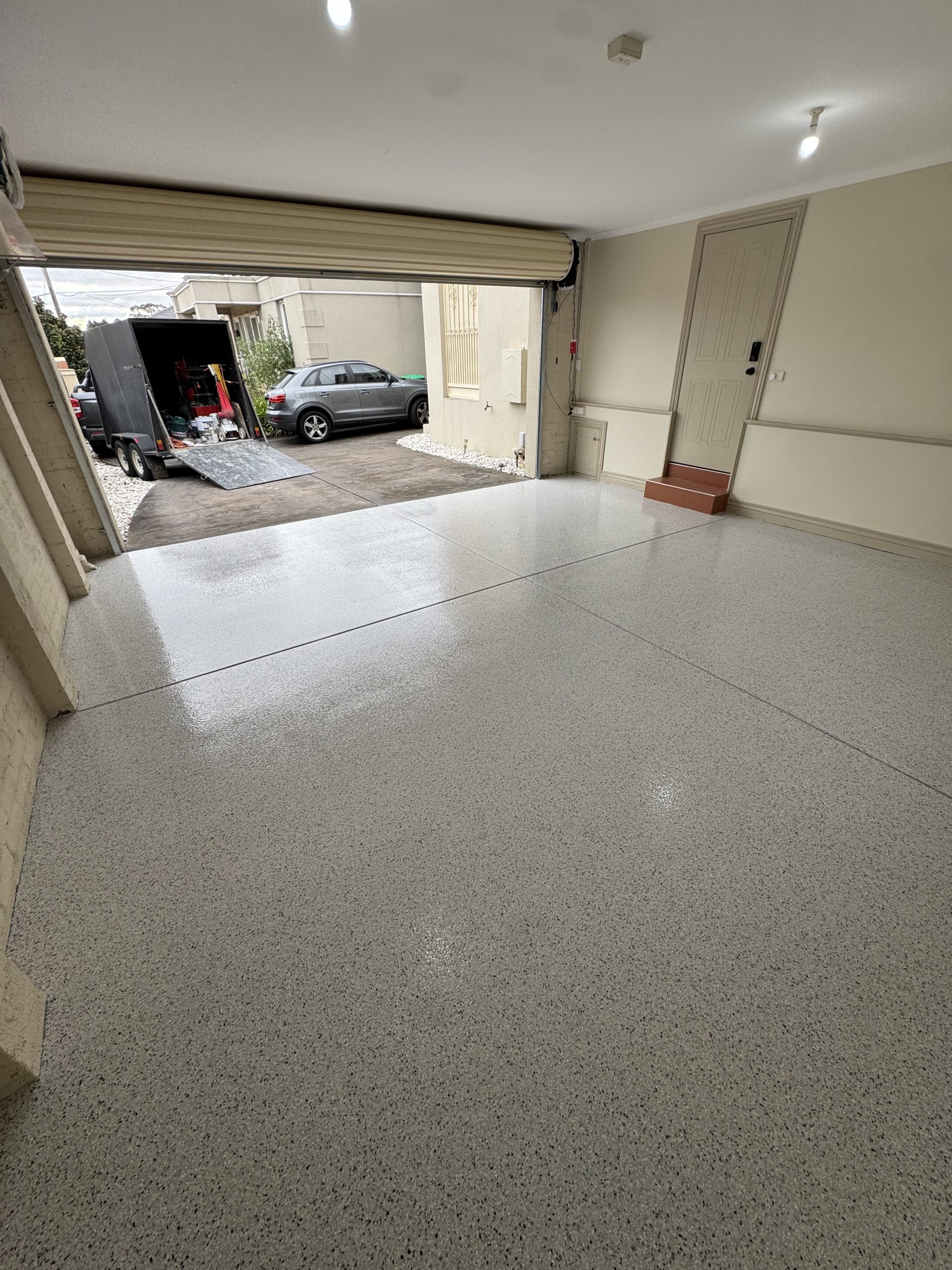 Spacious residential garage with glossy epoxy flake floor coating, open roller door, and driveway view