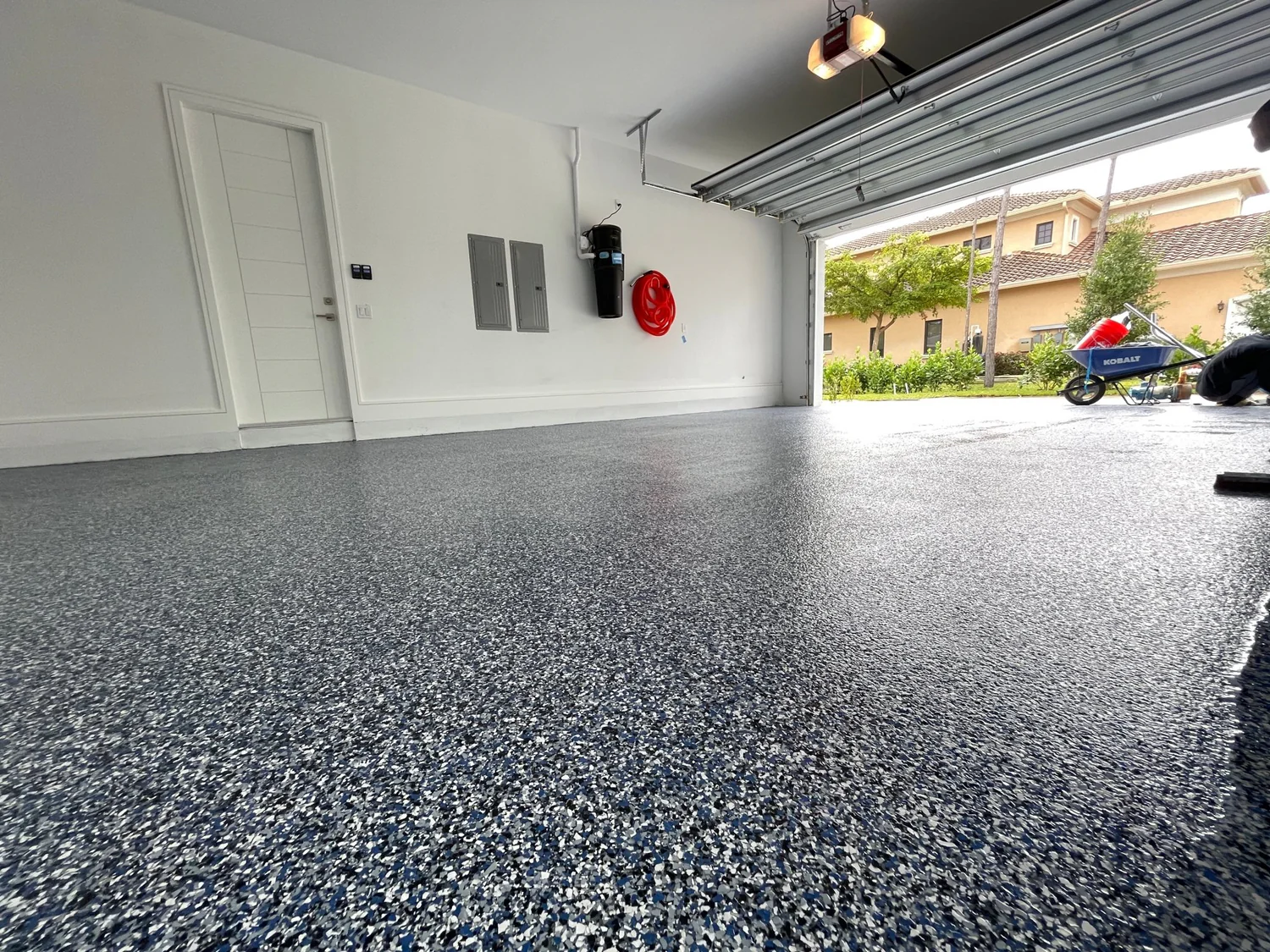 Garage with blue grey epoxy flake floor coating, white walls, open roller door and suburban street view