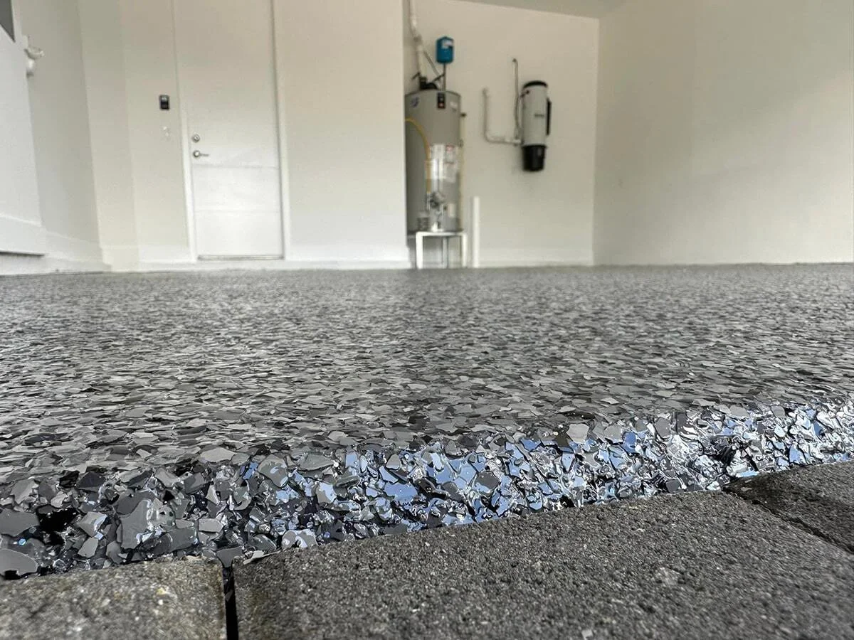Close-up edge of wet grey epoxy flake garage floor coating showing large fleck texture and glossy finish
